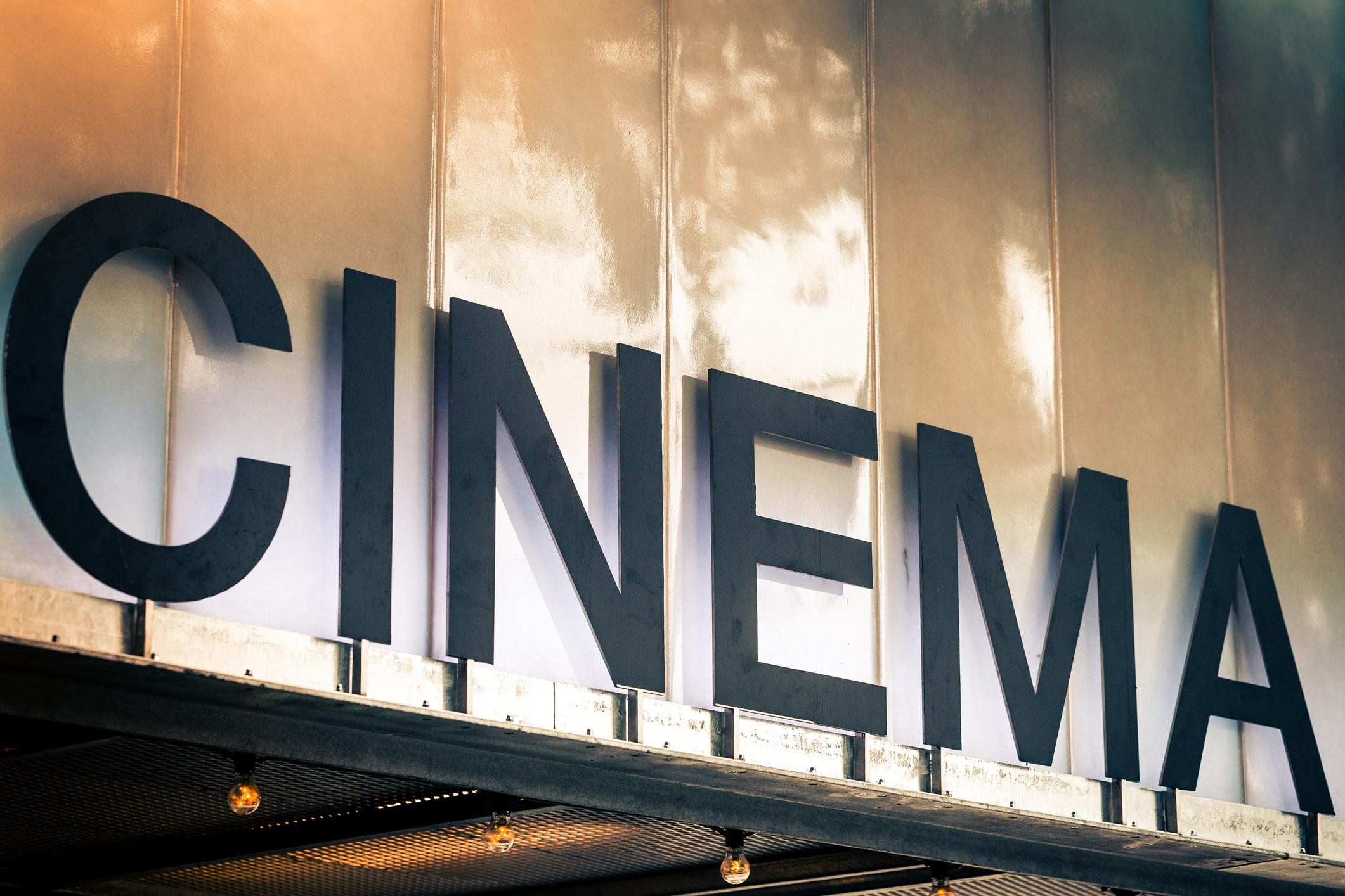 Color image depicting a sign saying 'cinema' in bold black capital letters outdoors in the city. Room for copy space.